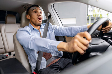 Dangerous traffic situation. Shocked black man driving, holding steering wheel and looking at road,...