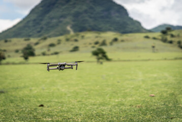 A high-tech drone hovering over a lush green field with a scenic mountain in the background....