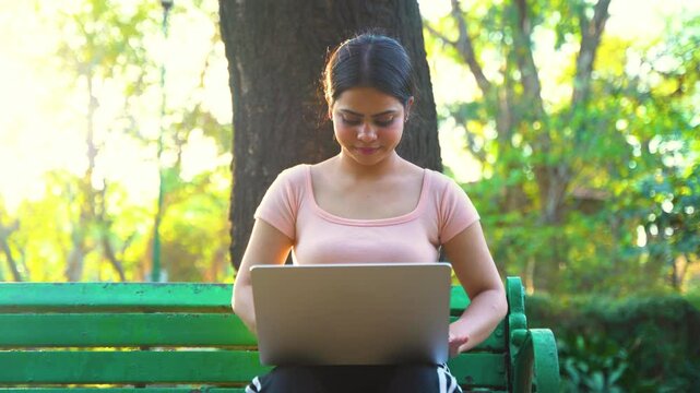 Young beautiful Indian woman working on a laptop sitting in the park, college student or business women remote work concept	