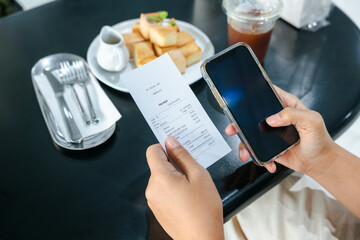 Closeup hands of a woman holding smart phone and food receipt, with toast and a cold drink on the...