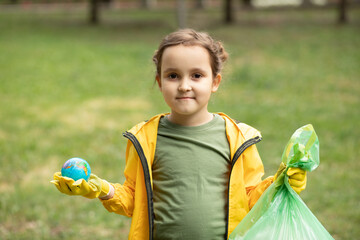 Child kid girl in a yellow raincoat holding globe in a one hand and plastic bag in the other hand. 