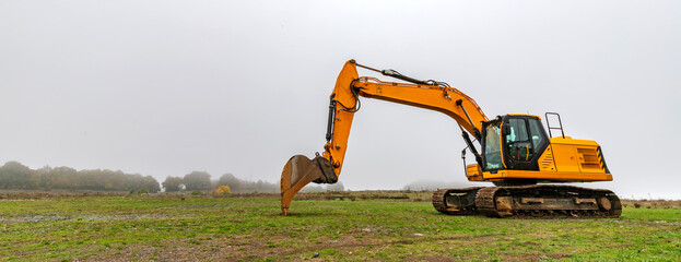 A yellow excavator parked in the meadow