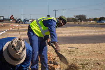 African road construction worker with a shovel digging a trench ditch on the side of the road, infrastructure repairs