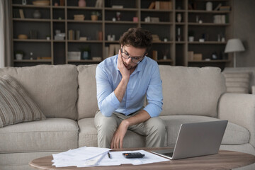 Financial problem. Stressed worried young businessman review documents using notebook calculator...