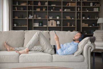 Peaceful moment and tech. Serene millennial male relax after work lying on comfortable sofa with...