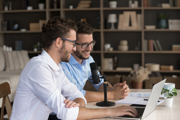 Digital tools in social media business. Team of two millennial twin brothers bloggers influencers using professional microphone notebook for recording podcast leading online webinar virtual meeting