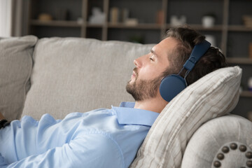 Chill vibes. Close up portrait calm tranquil young man relax in living room on comfy couch with...