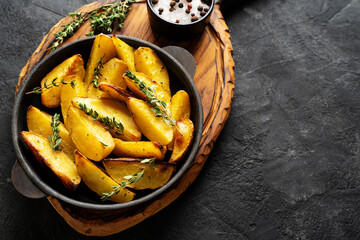 Roasted sliced potatoes with thyme herb, salt, peppers, cut board
