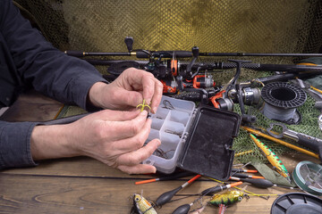 Sport fishing equipment on a table in a studio composition, against a background of a net. A fisherman's hands check the tackle for use.