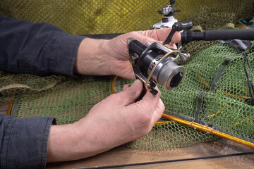 Sport fishing equipment on a table in a studio composition, against a background of a net. A fisherman's hands check the tackle for use.