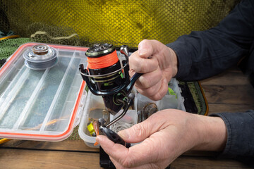 Sport fishing equipment on a table in a studio composition, against a background of a net. A fisherman's hands check the tackle for use.