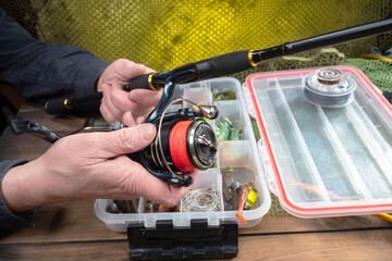 Sport fishing equipment on a table in a studio composition, against a background of a net. A fisherman's hands check the tackle for use.