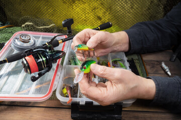 Sport fishing equipment on a table in a studio composition, against a background of a net. A fisherman's hands check the tackle for use.