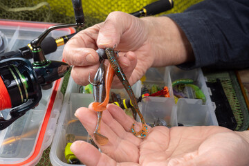Sport fishing equipment on a table in a studio composition, against a background of a net. A fisherman's hands check the tackle for use.