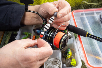 Sport fishing equipment on a table in a studio composition, against a background of a net. A fisherman's hands check the tackle for use.