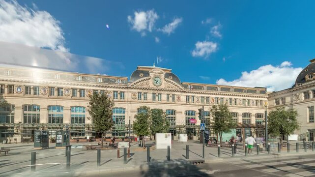 Monumental facade of Gare de Toulouse-Matabiau timelapse hyperlapse, featuring a clock, big windows and flags. The central railway station of Toulouse, France, under cloudy skies with road traffic