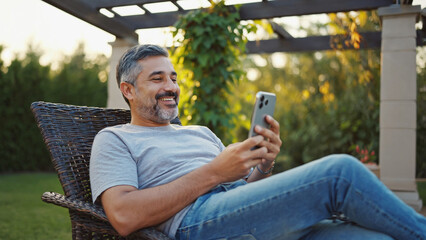 Contented Man with Phone: An image showing a man relaxing outdoors, using his smartphone. The scene exudes a sense of tranquility, with natural light and a peaceful atmosphere. 