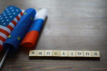 Sanctions Concept with USA, EU, and Russia Flags on Wooden Background with Scrabble Letters