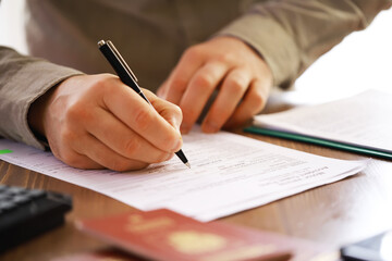 Close-Up of Person Filling Out Forms with Passport and Pen on Table