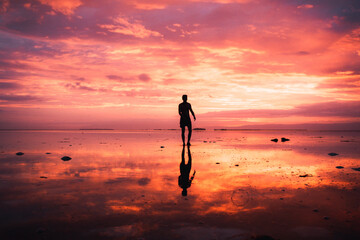  A man's silhouette standing on the beach in front of a beautiful sunset with stunning reflections on the water. Panglao, Bohol Sunsets.