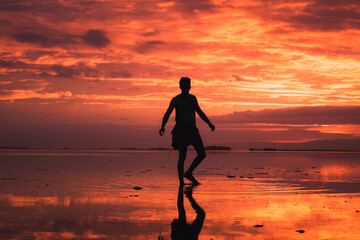 A Man's silhouette dancing freely on the beach, in a stunning, orange sunset, with incredible reflection of the sunset colors. Panglao, Bohol Sunsets.