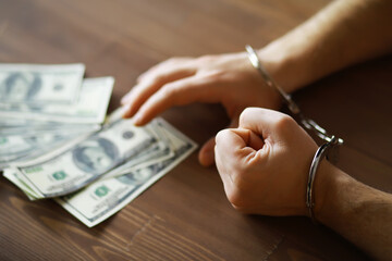 Handcuffed Hands Touching Dollar Bills on Wooden Table - Financial Crime Concept