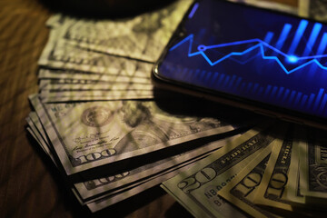Financial Success: Smartphone with Stock Market Graph on Screen and Stacks of US Dollar Bills