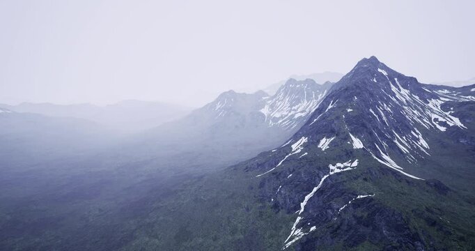 Layers of majestic mountains dominate the landscape, covered with patches of snow. Mist envelops the peaks, lending an ethereal quality to the lush green valley below.