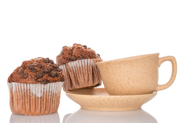 Two chocolate cupcakes on a ceramic saucer with a cup, isolated on a white background, close-up.