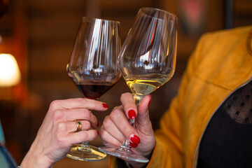 Two women clink glasses of red and white wine in a cozy setting. A perfect moment for a romantic...