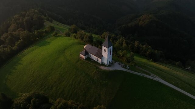 Pull-back drone shot of the Saint Primus and Felician Catholic Church at sunset in Jamnik, Slovenia