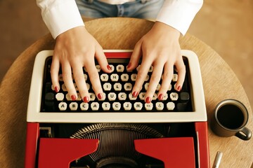 Woman typing on a vintage red typewriter with coffee cup on wooden table in warm light background, symbolizing retro writing and blogger creativity.