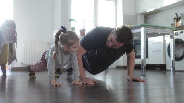Father and daughter doing push-ups together at home, enjoying fun exercise time.