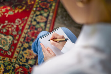 Obraz premium Woman in white shirt and blue pants writing with pen in notebook, psychologist, teacher. Top view of woman with notebook and pen, journalist or psychologist making notes on paper
