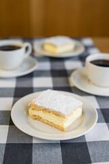 Kremówka i filiżanki kawy na biało-czarnym obrusie, apetyczne ujęcie deseru