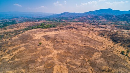 Fototapeta premium Aerial View of Dry Cracked Land with Mountains on Horizon in Arid Climate with Geological Formations Carved by Water Erosion