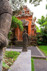 A serene Buddhist statue faces an ancient Balinese temple surrounded by lush greenery, showcasing...