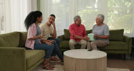 Opening gift box, elderly diverse couple surrounded by smiling family during gathering, at home
