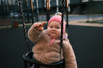 Child is having fun swinging in a park while wearing a pink hat and cozy outfit The bright morning...