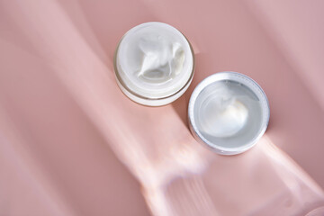 An open jar of cream with its texture on a pink background.