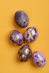 Happy Easter day! Сomposition with modern Easter eggs with gold decorations and spring flowers on yellow background. Easter holiday background with stylish eggs decorations. Flat lay, copy space.