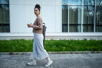 University student walking on campus with coffee and backpack
