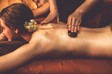 Hot stone massage at spa salon in luxury resort with warm candle light, blissful couple customer...