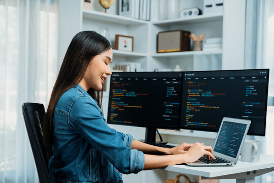 Smiling young Asian in IT developer creating with typing online information on laptop with coding program data of application, wearing jeans shirt. surrounded by safety analysis two screen. Stratagem.