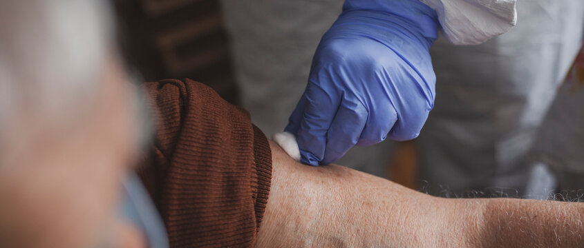 Doctor in protective suit vaccinating elderly man at home during epidemic