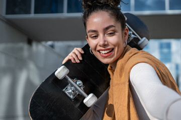 Smiling skater holding skateboard taking selfie in urban city