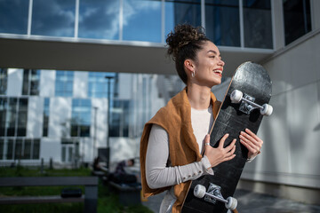 Happy stylish woman holding skateboard smiling near modern building