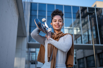 Stylish businesswoman holding skateboard in front of modern office building