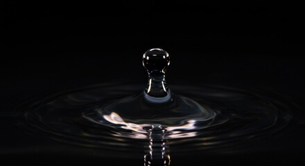 A single water droplet captures and refracts light, creating a stunning visual effect against a dark background