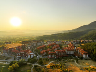 Warm golden hues cover Bansko, Bulgaria, as sun rises over mountain peaks. Aerial view showcases...